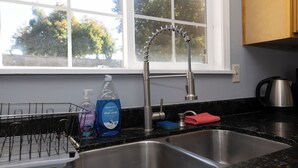 A kitchen with a double sink, a dish soap bottle, a dish rack, and a window with a view of trees. - Family and Business Friendly Home near Great Mall & BART - 2640 (San Jose)