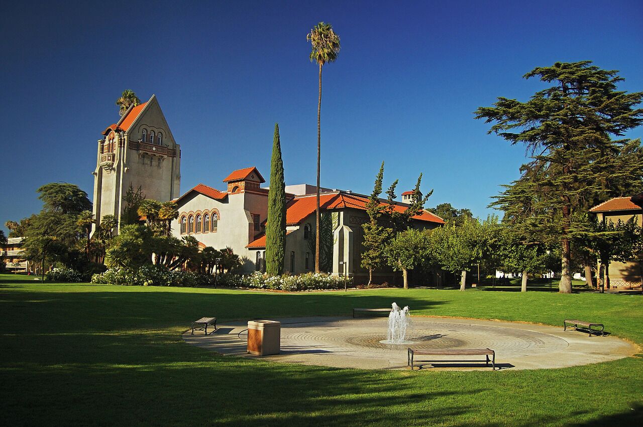 A historic building with a tower, surrounded by a well-maintained lawn and a fountain.