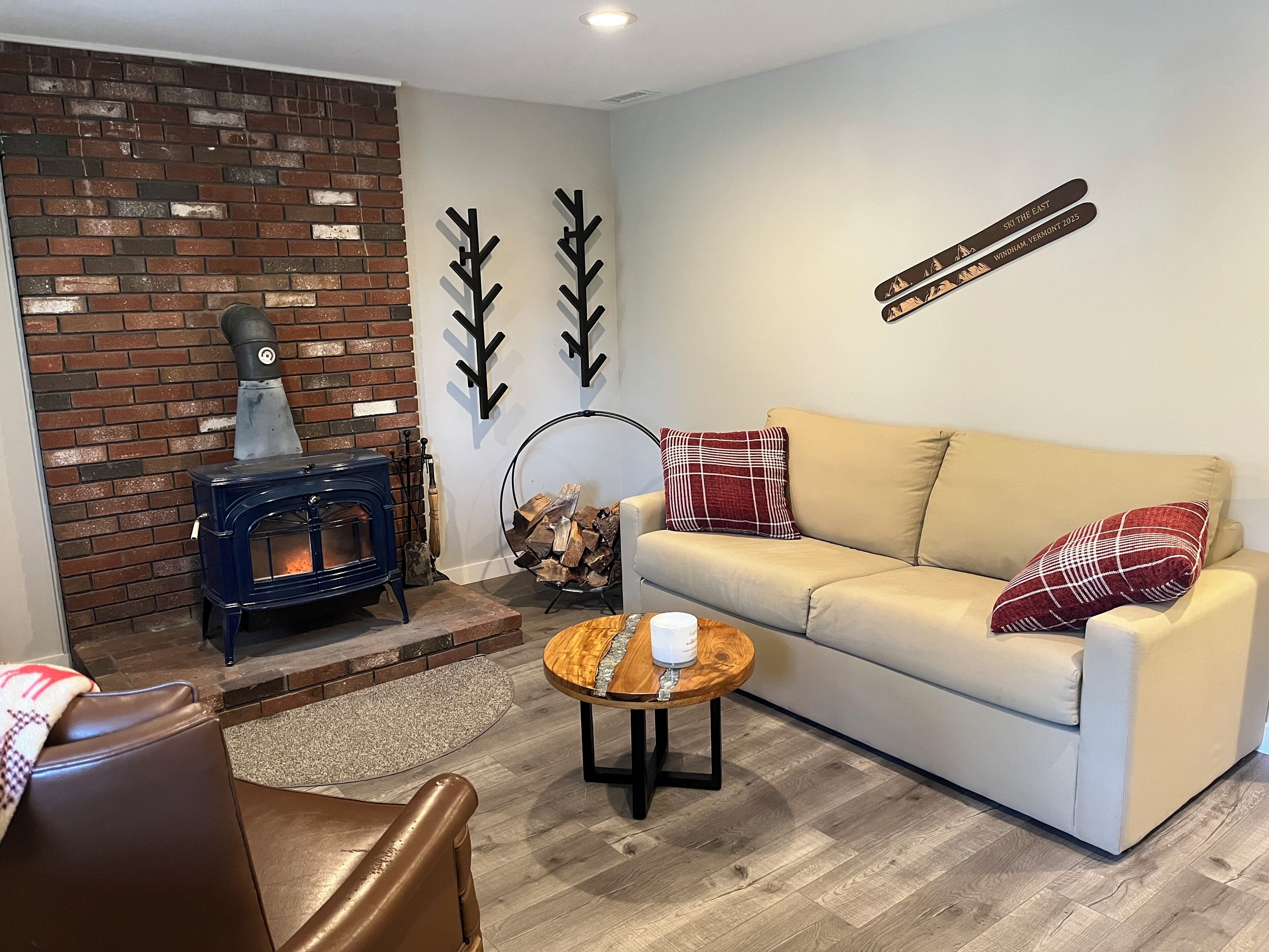 A cozy living room with a brick wall, a blue wood-burning stove, a beige sofa, and a coffee table.