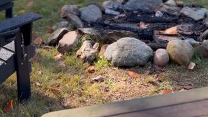Un terrain de camping avec un foyer entouré de rochers, une chaise Adirondack noire et une table de pique-nique.