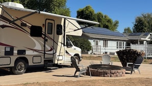 A recreational vehicle parked in a driveway with a fire pit and outdoor seating. - Cozy RV stay on a South Gilbert Mini Farm (Gilbert)