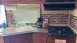 A compact kitchen with wooden cabinets, a microwave, a stove, and a sink. - Cozy RV stay on a South Gilbert Mini Farm (Gilbert)