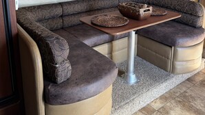 A cozy seating area with a cushioned bench and a small table, a decorative wall piece, and a ceiling-mounted light fixture. - Cozy RV stay on a South Gilbert Mini Farm (Gilbert)
