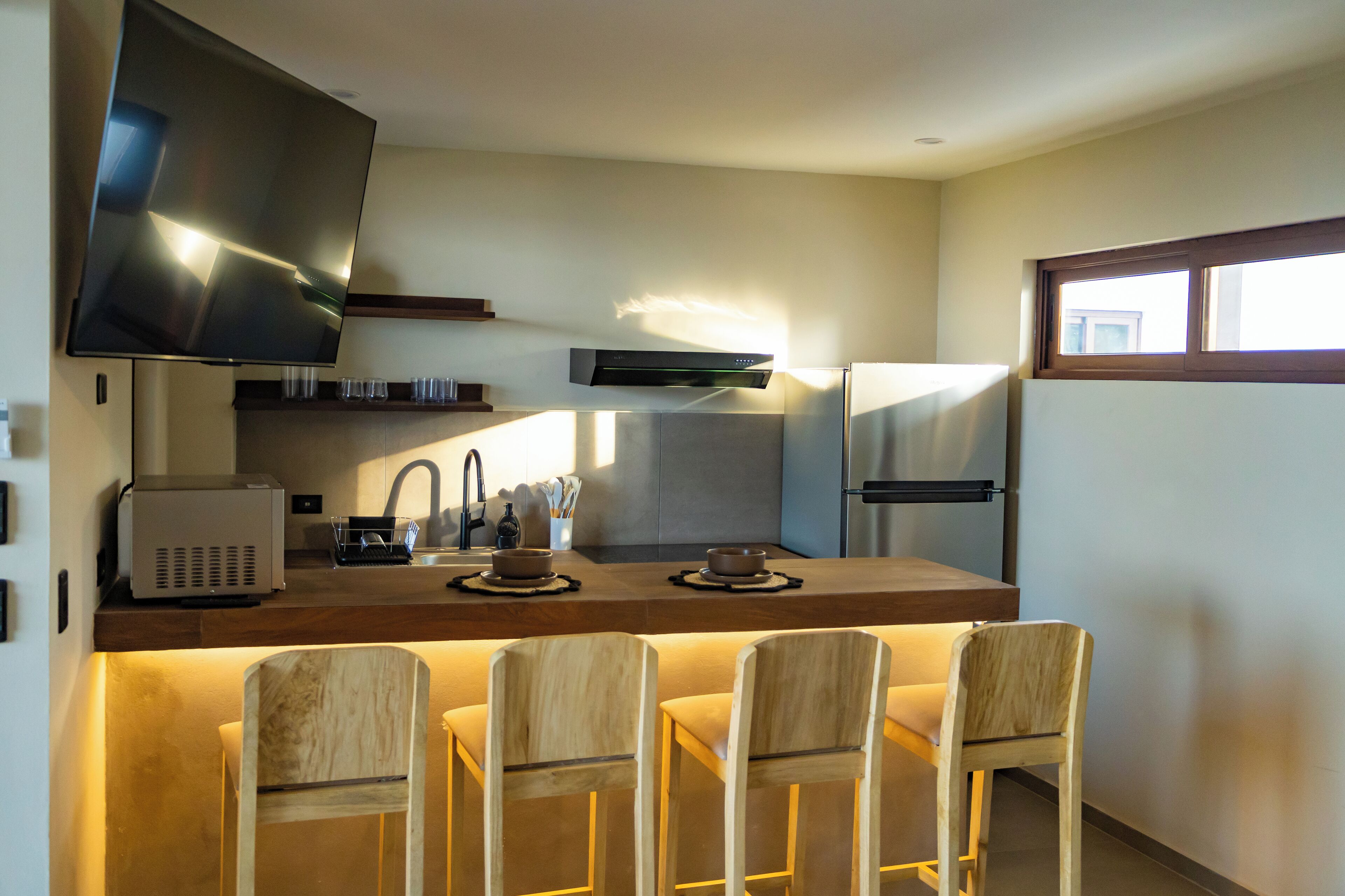 Una cocina moderna con televisión de pantalla plana, horno integrado y un comedor con cuatro sillas de madera.