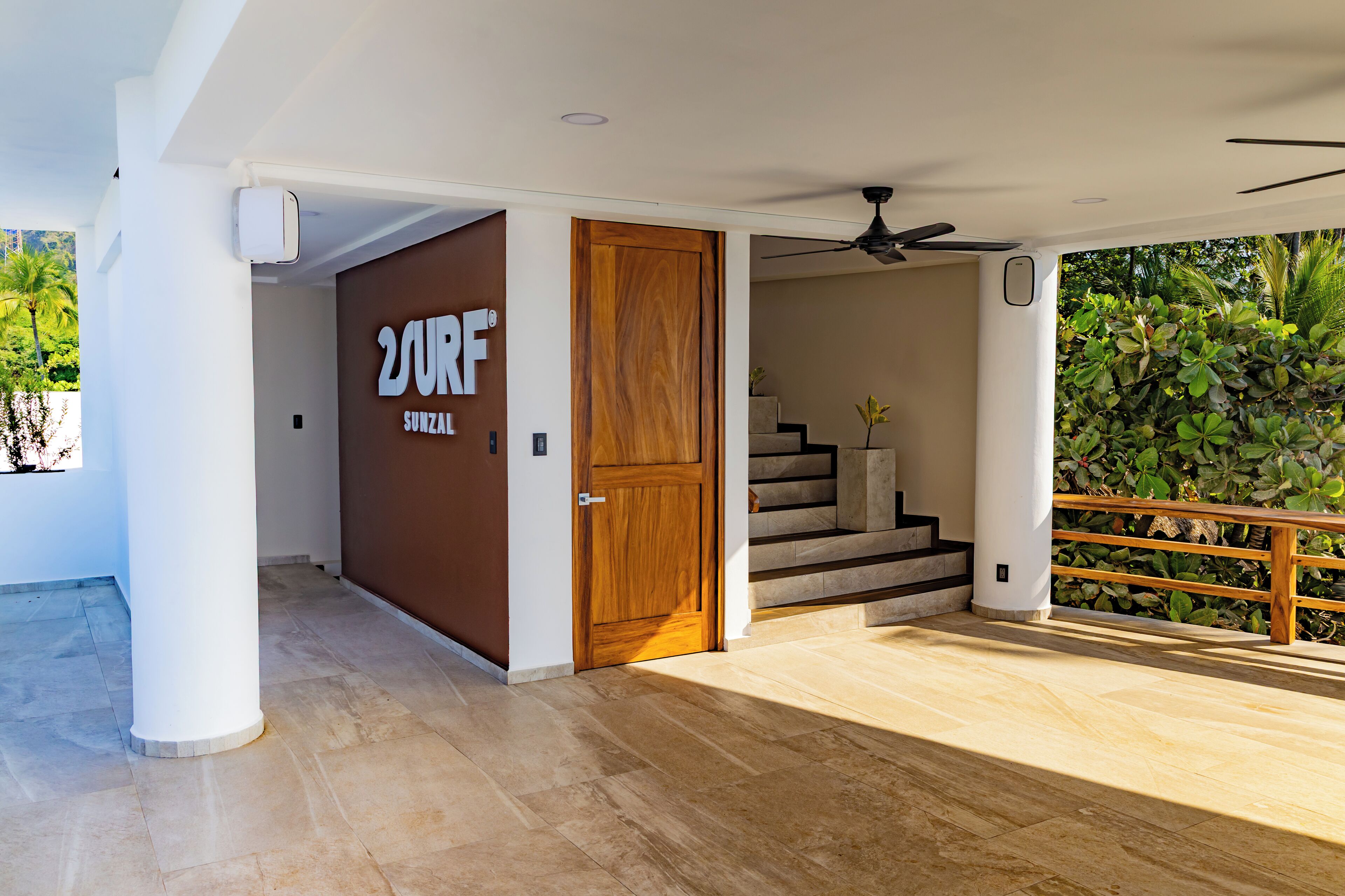 A modern interior with a wooden door labeled "SURF" and a staircase leading to an outdoor area with a wooden railing and greenery.