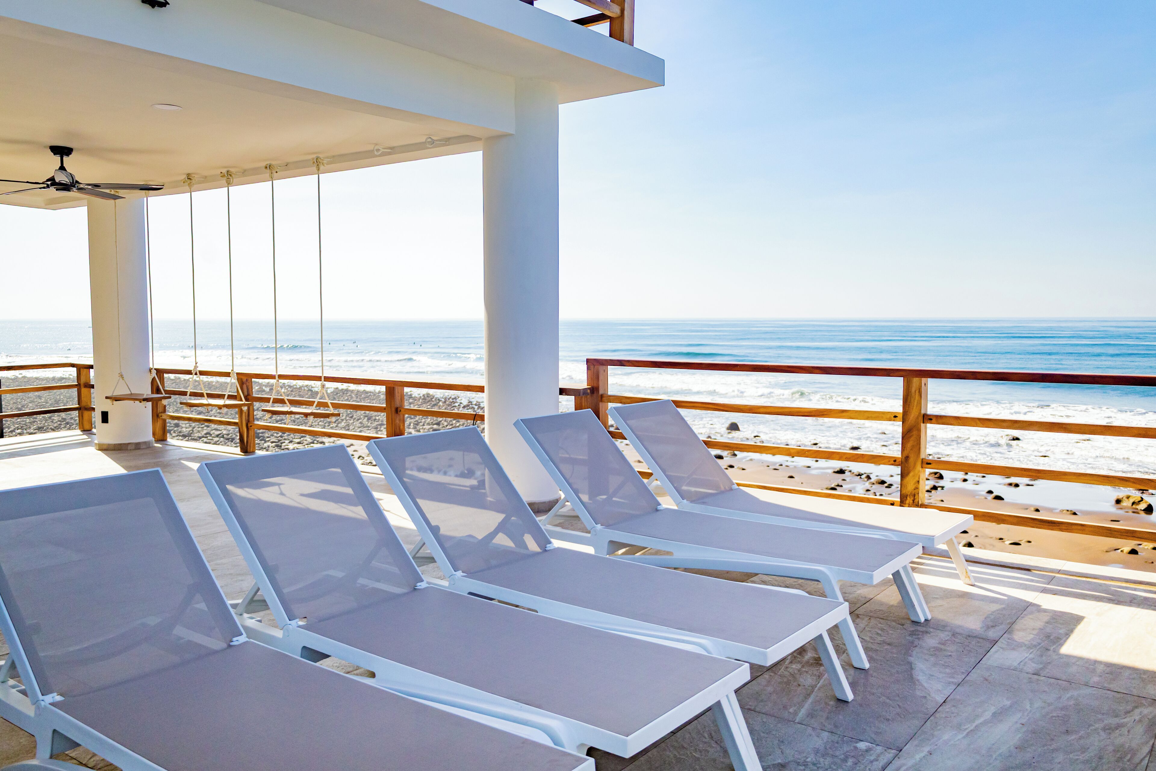 Un espace extérieur aménagé, abrité, avec des fauteuils blancs et une vue sur la plage.