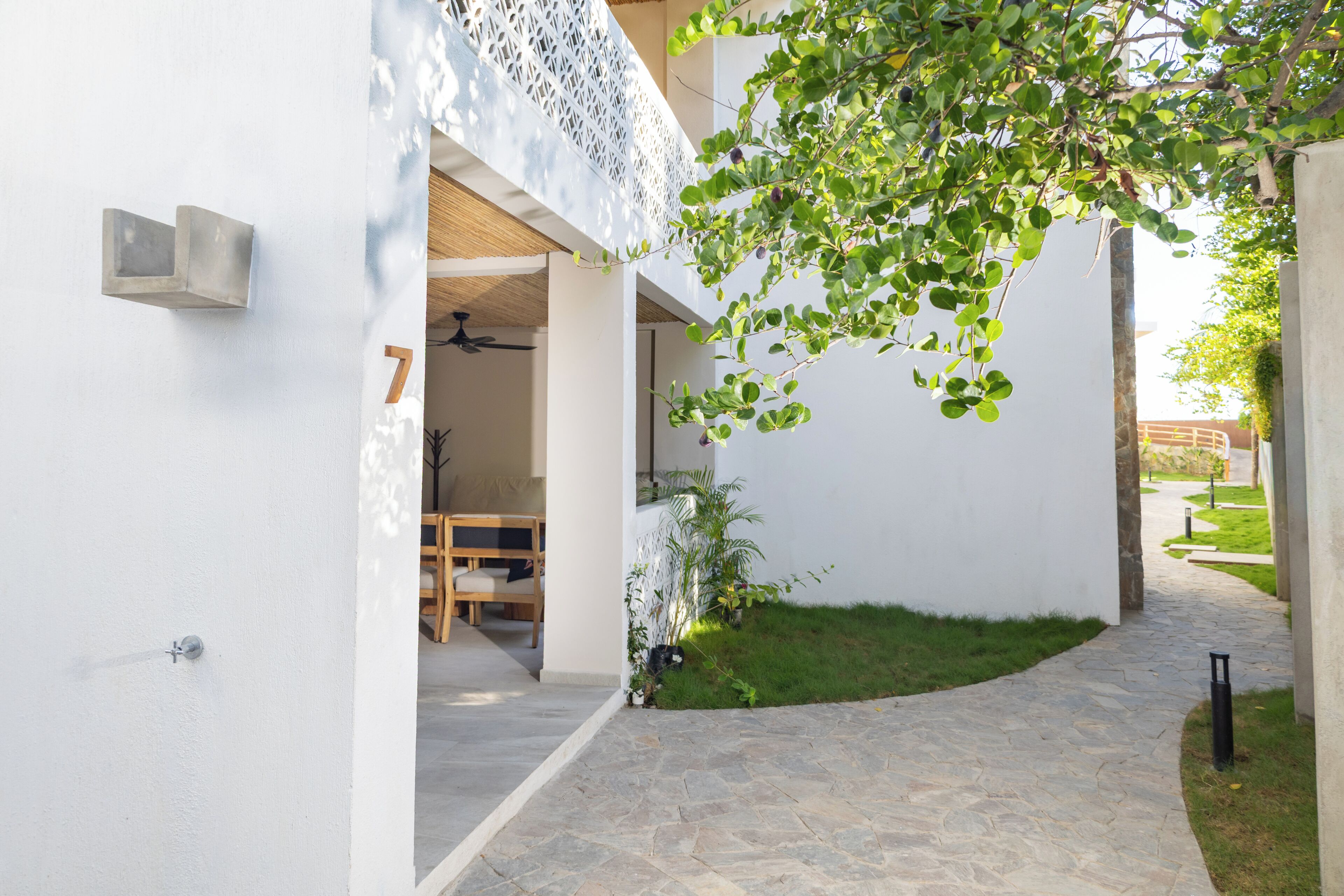 Un espacio exterior moderno con un sendero de piedra, un banco de madera y un pequeño jardín con un árbol.