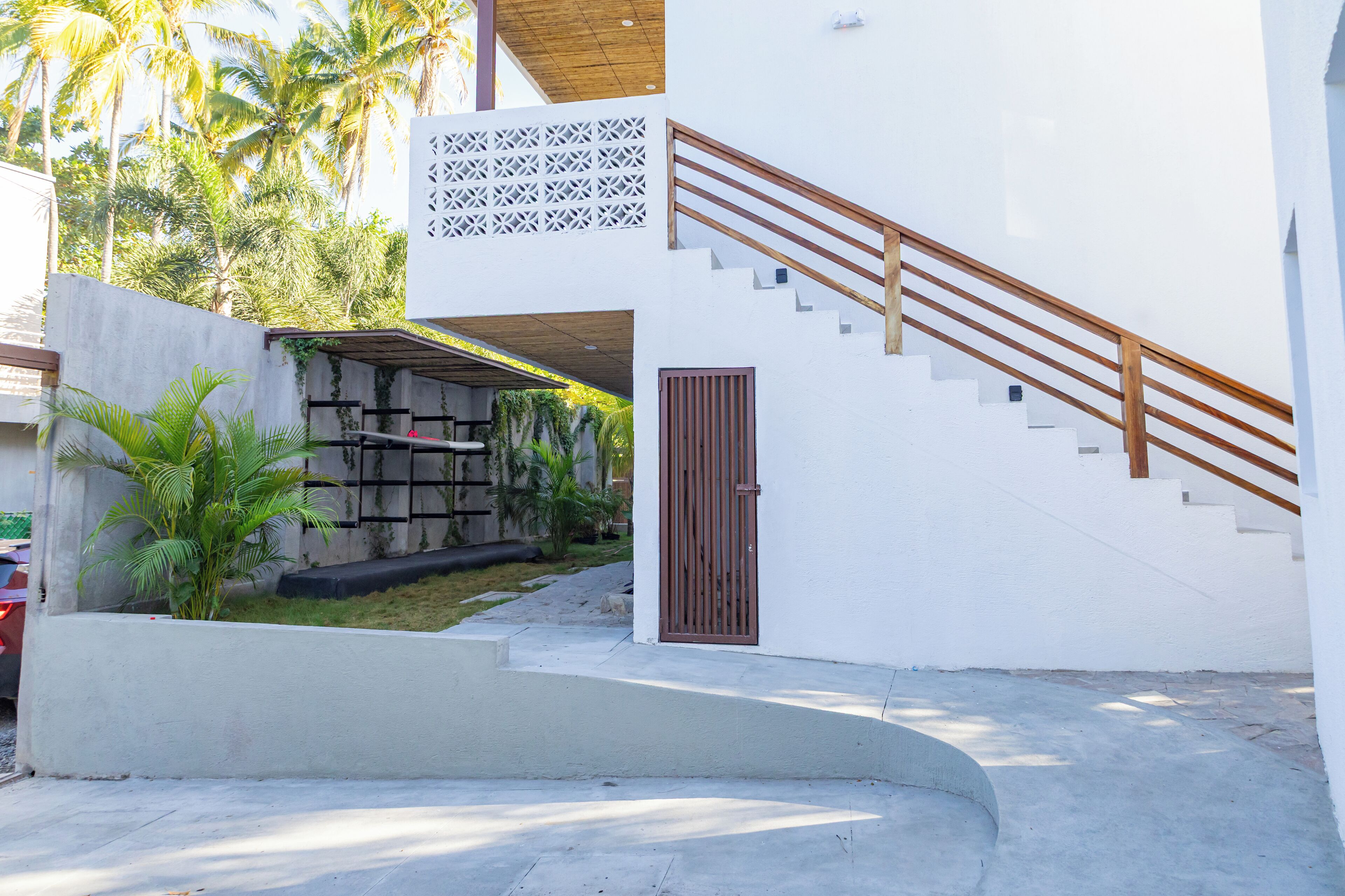Un edificio moderno con una escalera, una entrada protegida por un portón y un área exterior cubierta con plantas.
