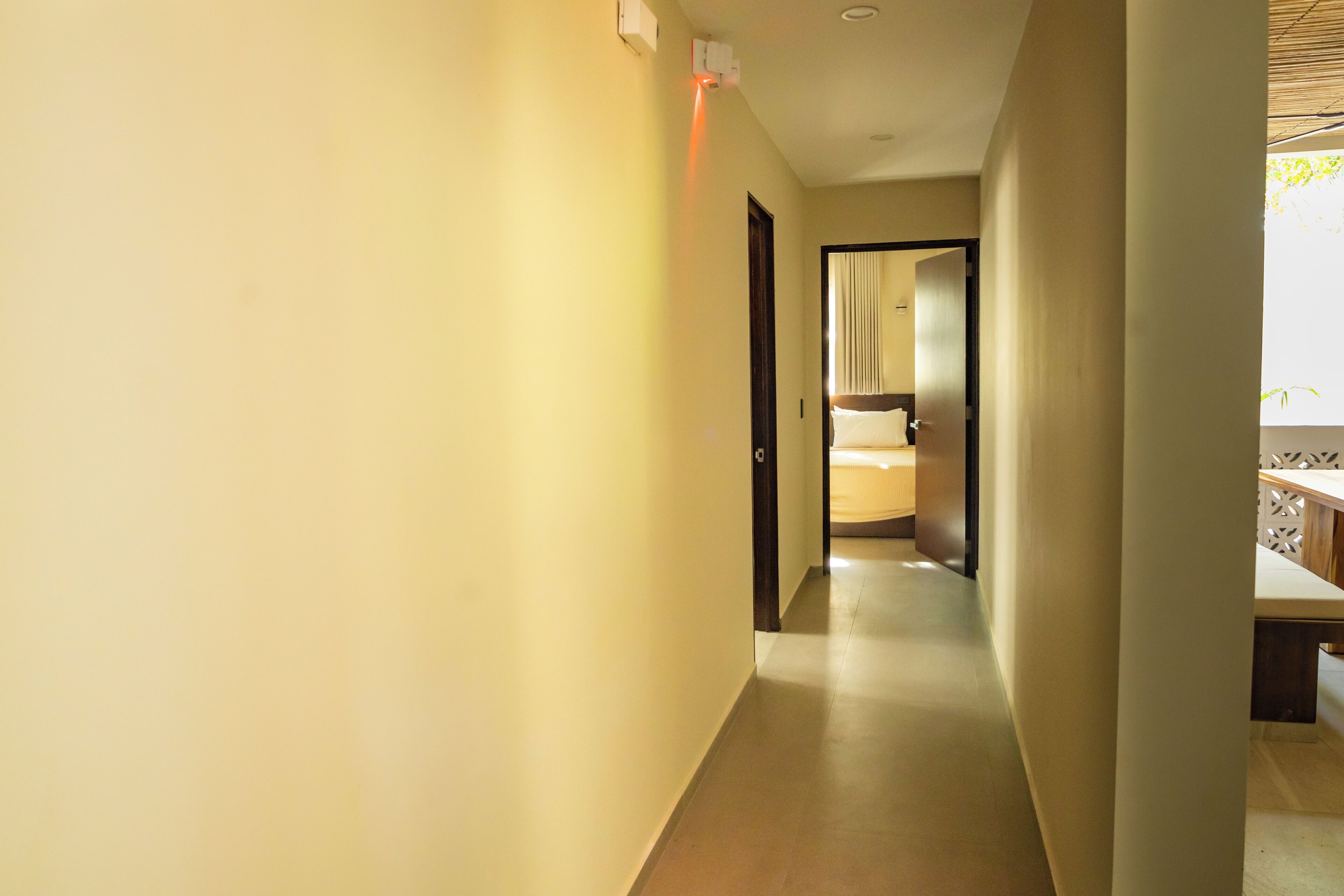 Un couloir d’hôtel avec un lit en arrière-plan, une porte sur la droite et un luminaire fixé au mur.