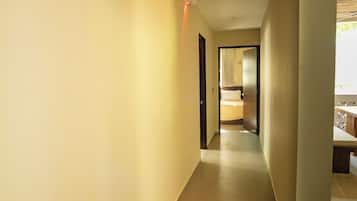 Un pasillo de hotel con una cama al fondo, una puerta a la derecha y una lámpara en la pared.