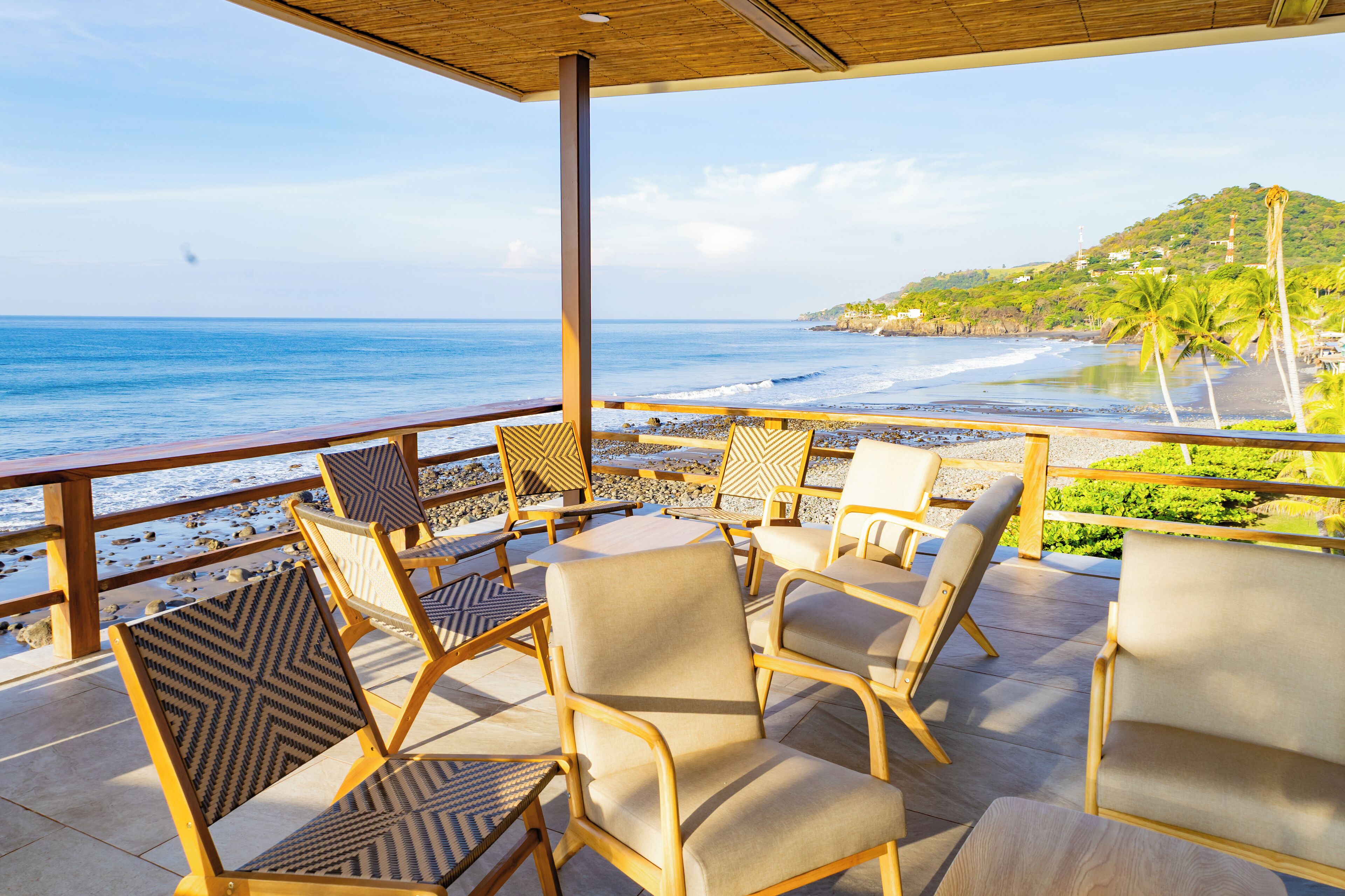 A covered outdoor seating area with chairs and tables overlooking a beach.