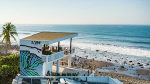 Un edificio frente a la playa con un mural, asientos al aire libre y vistas al océano.