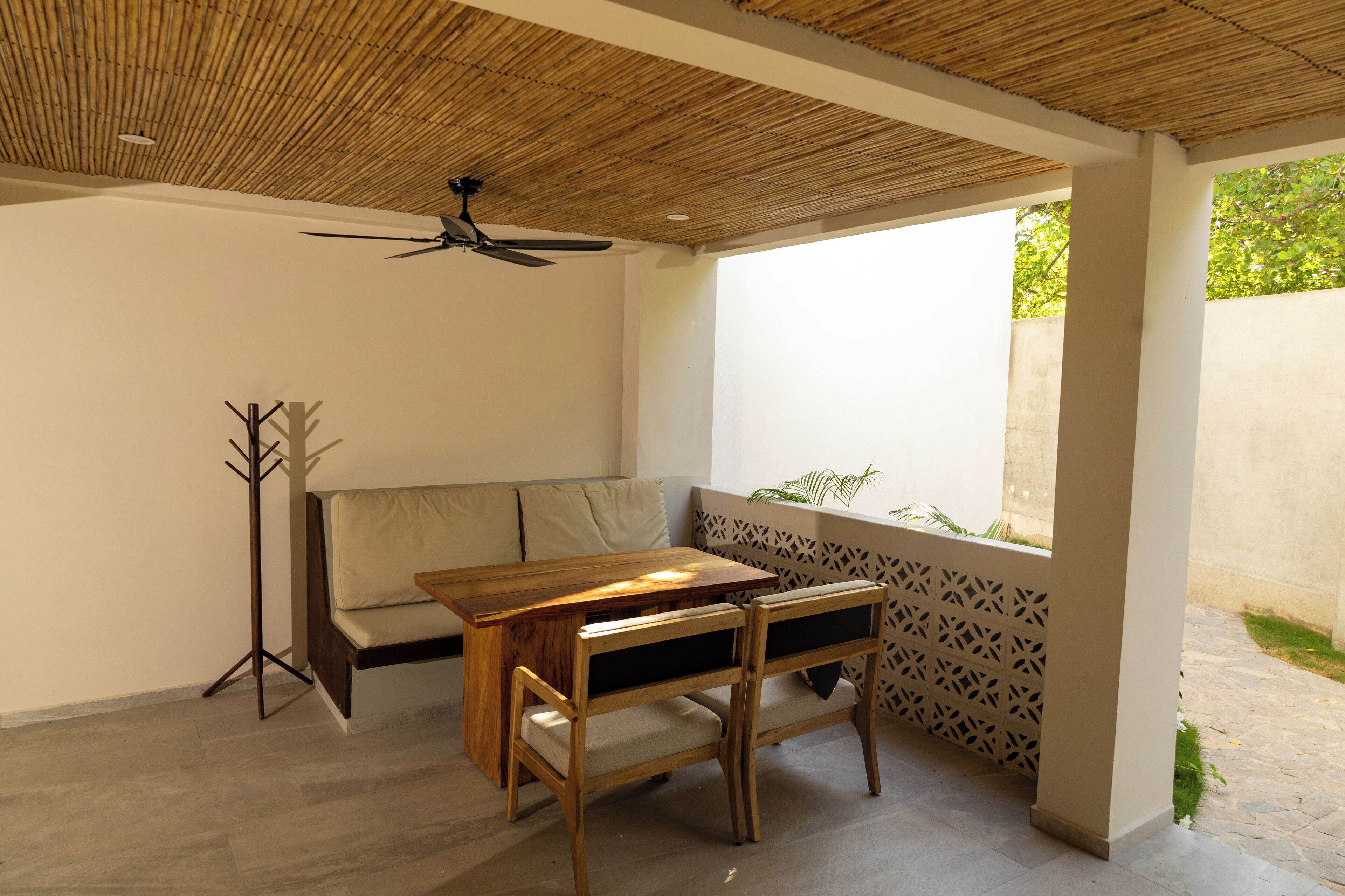 Une pièce avec une table et des chaises en bois, un canapé, un ventilateur de plafond et un mur orné d’un motif.