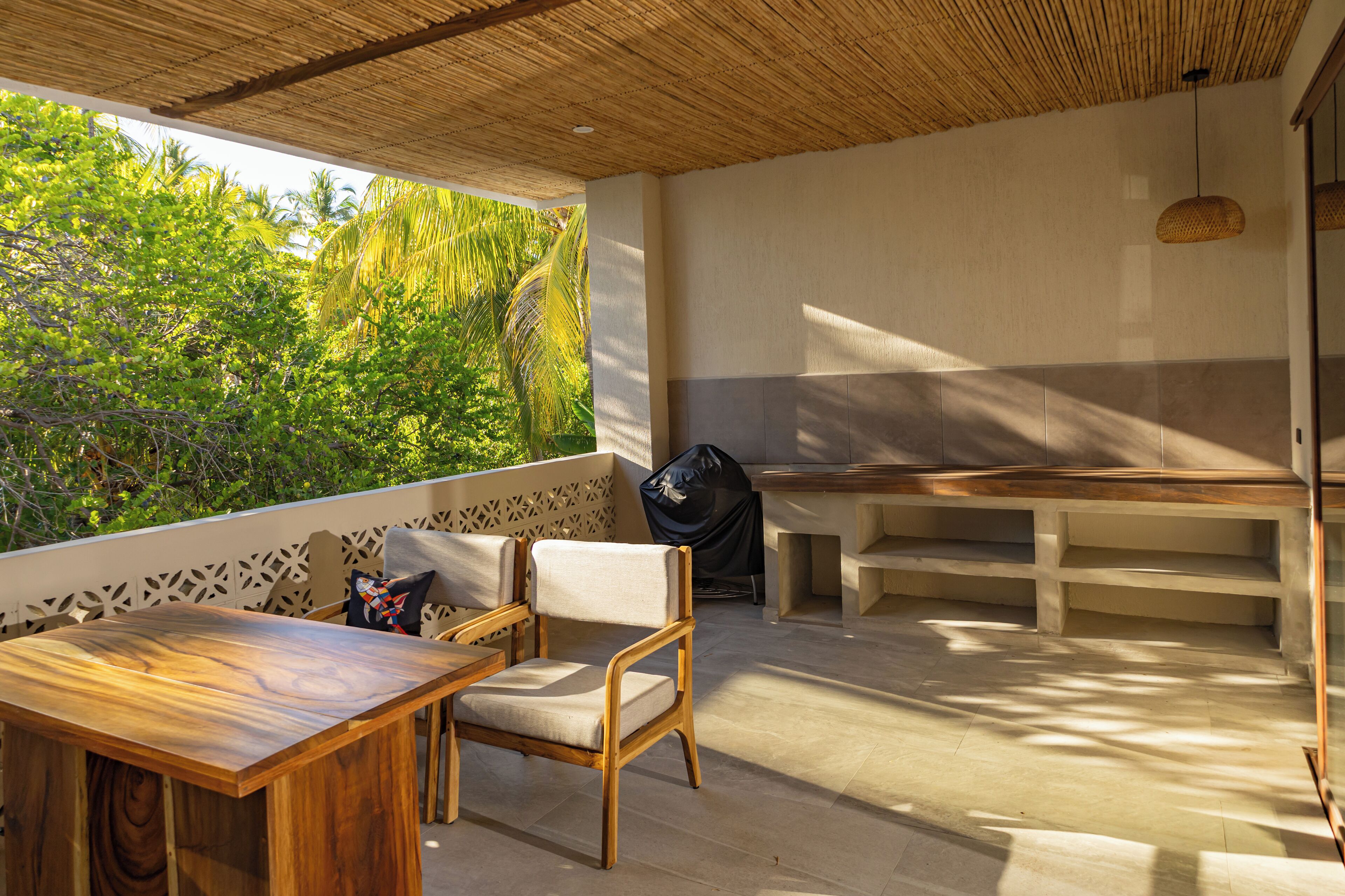 Un patio con mesa y sillas de madera, una parrilla y vistas a vegetación exuberante.