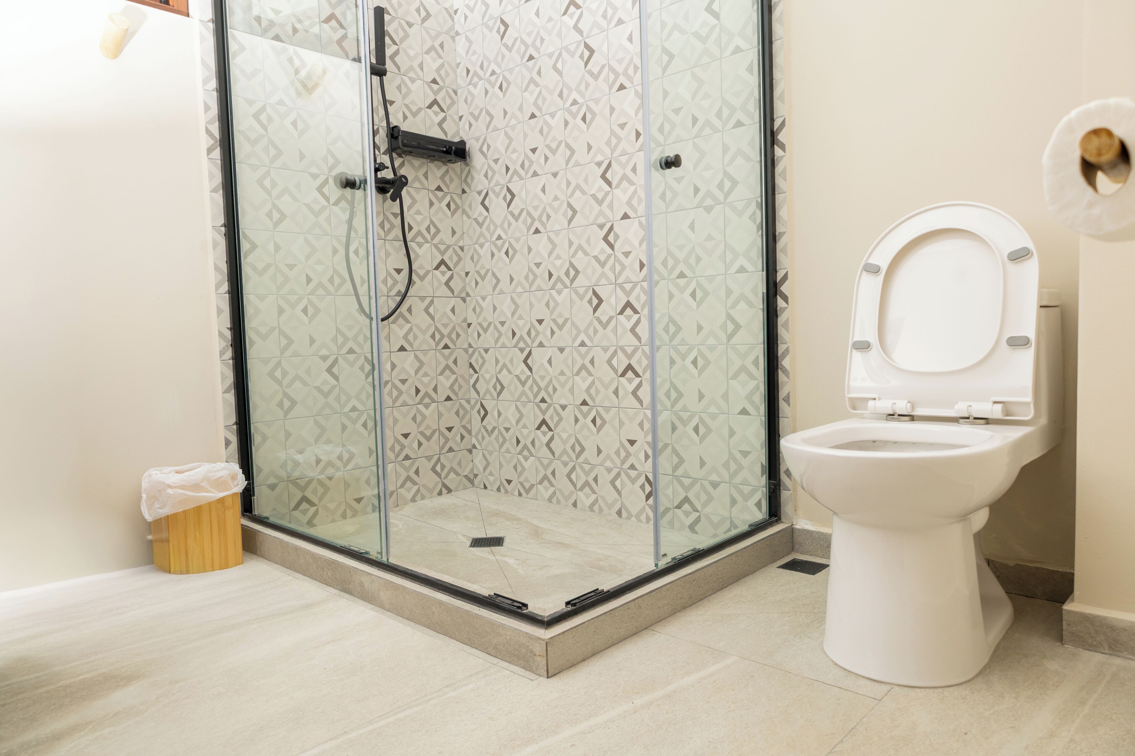 Un baño moderno con ducha de vidrio, inodoro blanco y azulejos estampados.