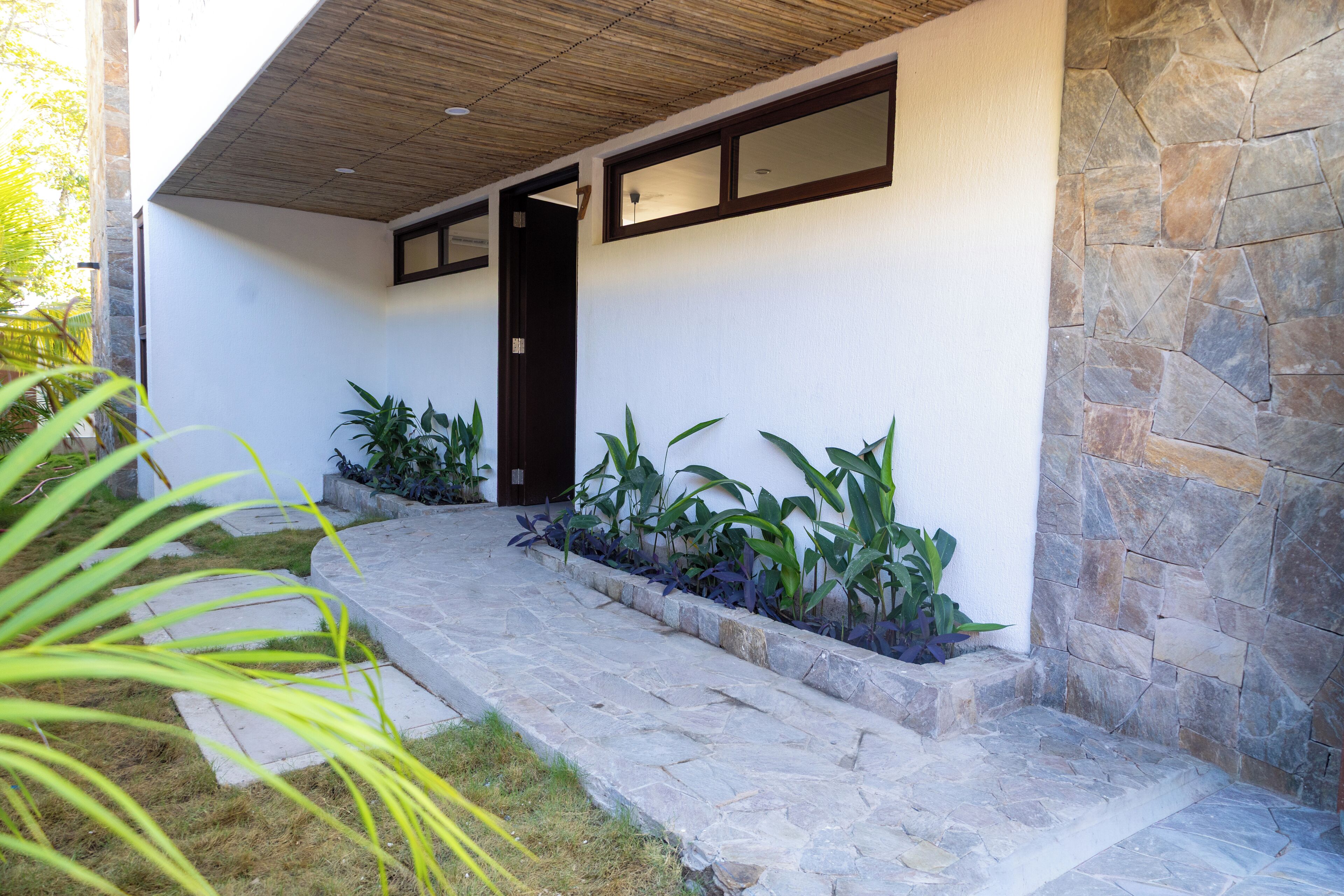 A modern building with a stone facade, a wooden ceiling, and a stone staircase leading to a dark door.