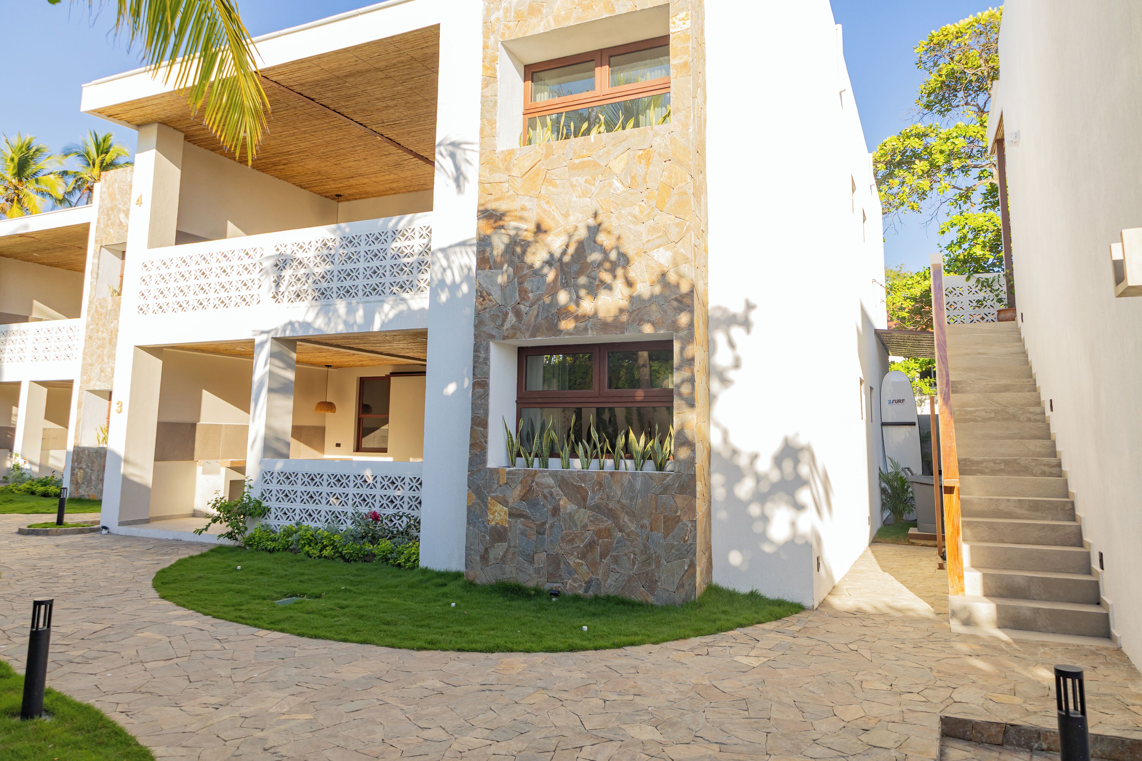 A modern building with a stone facade, a wooden balcony, and a paved courtyard.