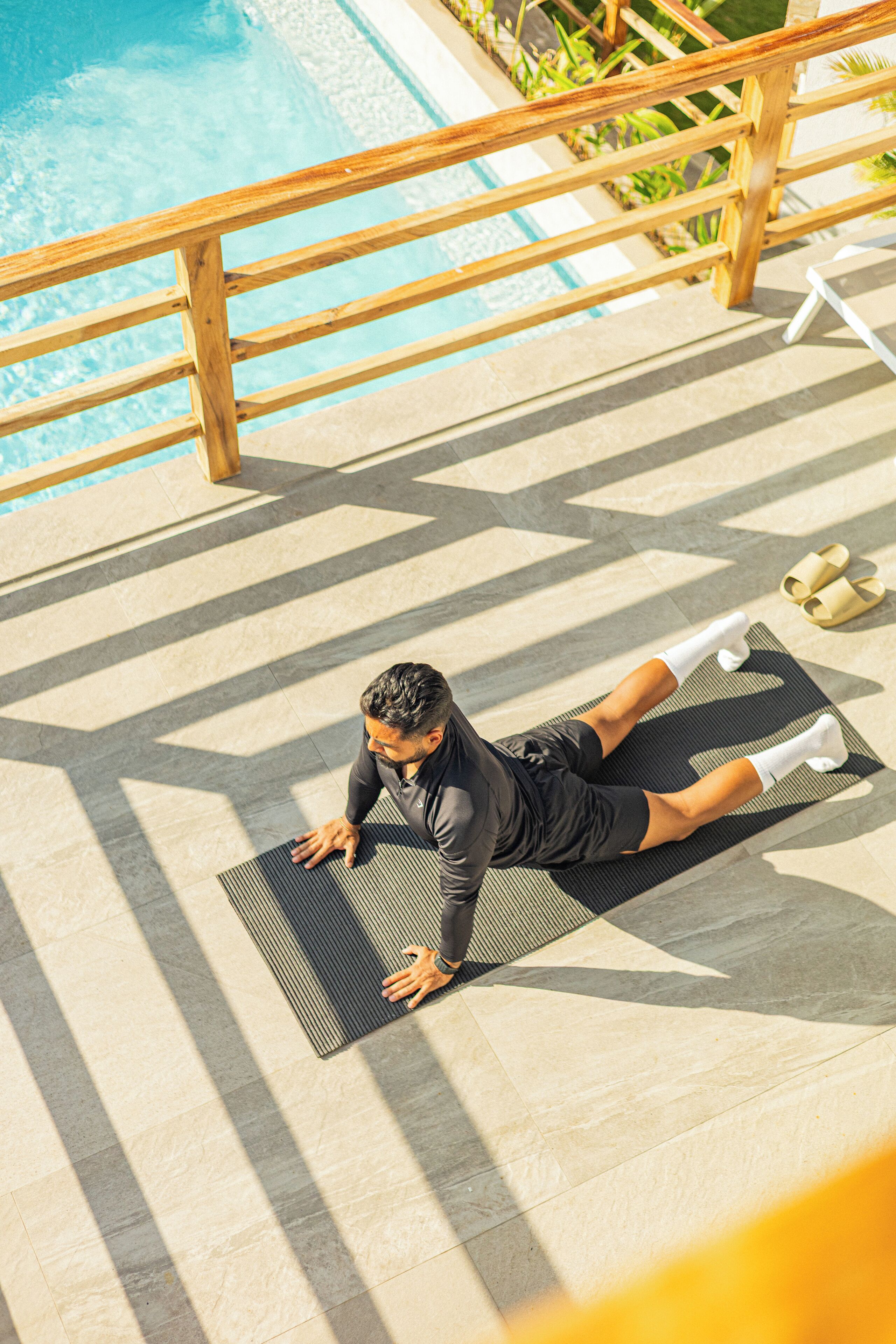 Une personne effectue un exercice d'étirement sur un tapis, près d'une piscine.