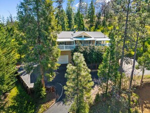 A two-story lodge with a covered deck and a garage, surrounded by dense forest. - 5BR Pine Mountain Lake Retreat | Near Yosemite (Groveland)