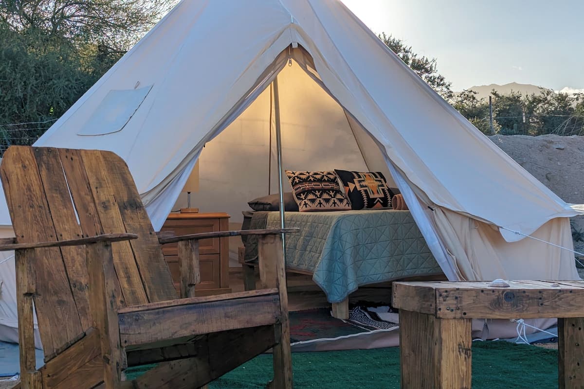 Une tente avec un lit à l’intérieur, entourée de meubles en bois et d’un tapis vert.
