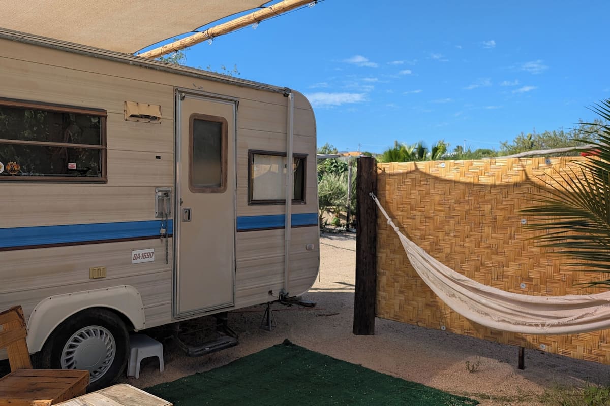 Un camping-car est garé à côté d’un mur fait de bambou tressé, et un hamac y est attaché.