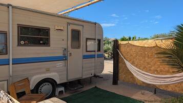 Una autocaravana estacionada junto a una pared de bambú tejido, con una hamaca atada a ella.