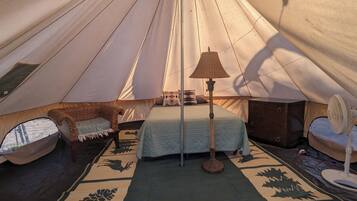 Een gezellig ingerichte tent met een bed, een stoel, een kastje en een ventilator.