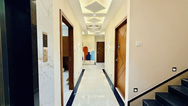 A modern hotel hallway with a marble floor, wooden doors, and a geometric ceiling design. - Hotel Mantri Ji (Ujjain)