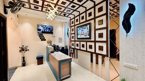 A reception area with a modern design, featuring a reception desk, a mounted television, and framed artwork on the walls. - Hotel Mantri Ji (Ujjain)