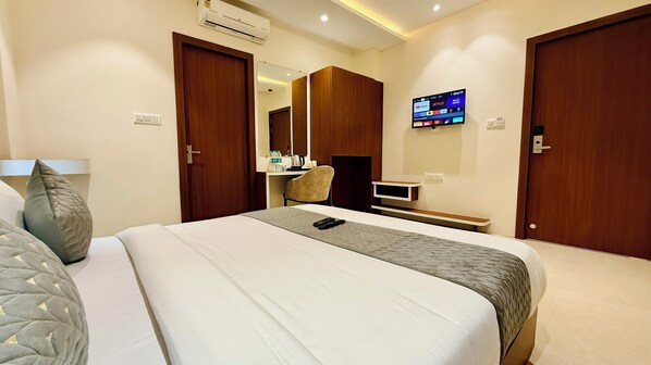 A hotel room with a bed, a desk, a chair, a TV, and a wardrobe. - Hotel Mantri Ji (Ujjain)