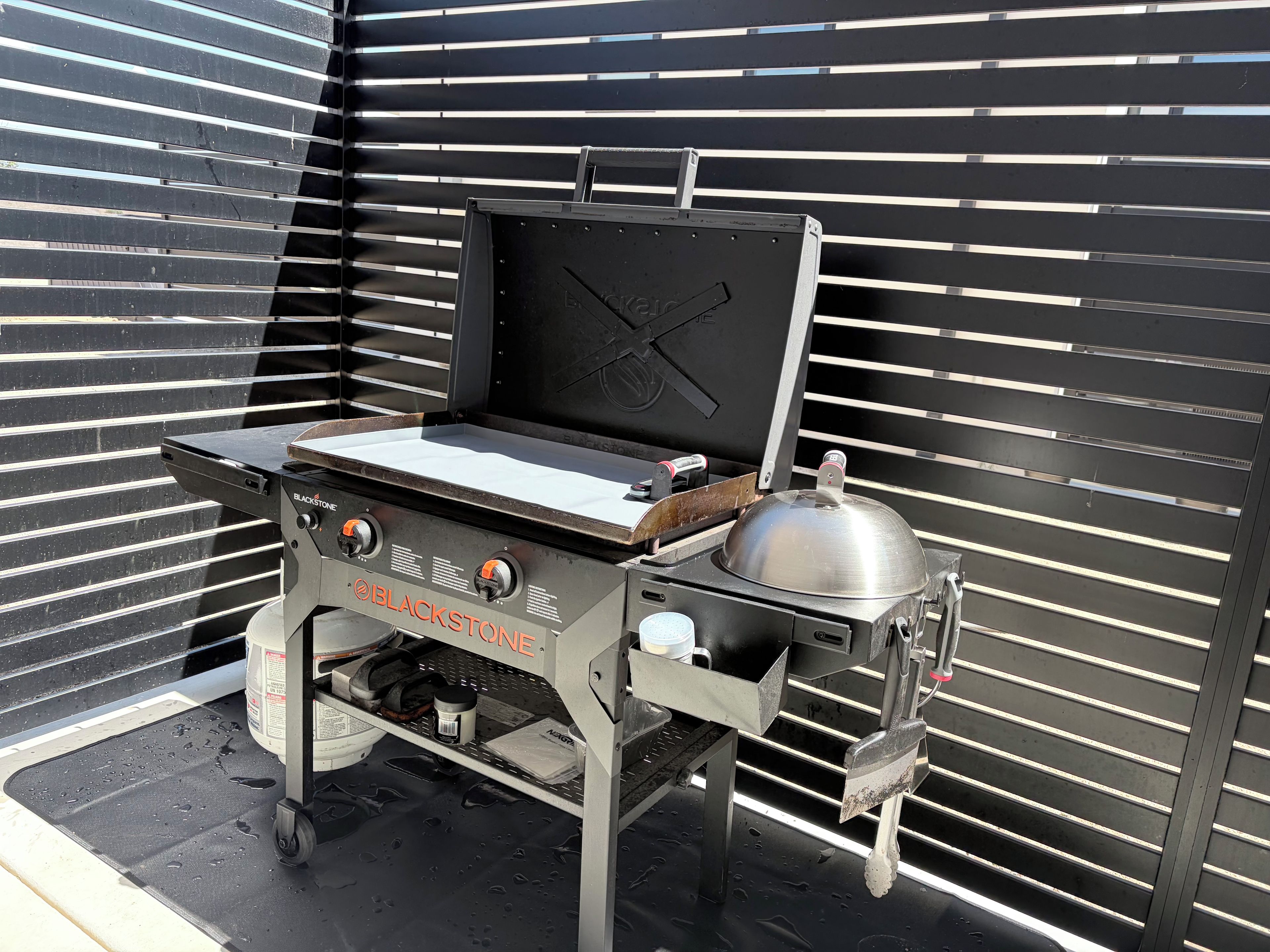 A portable grill with a lid, control knobs, and a metal pot on a wheeled stand.