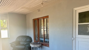 Una habitación con piso de baldosas, un sillón de cuero, una mesita, una ventana con persianas y una puerta blanca.
