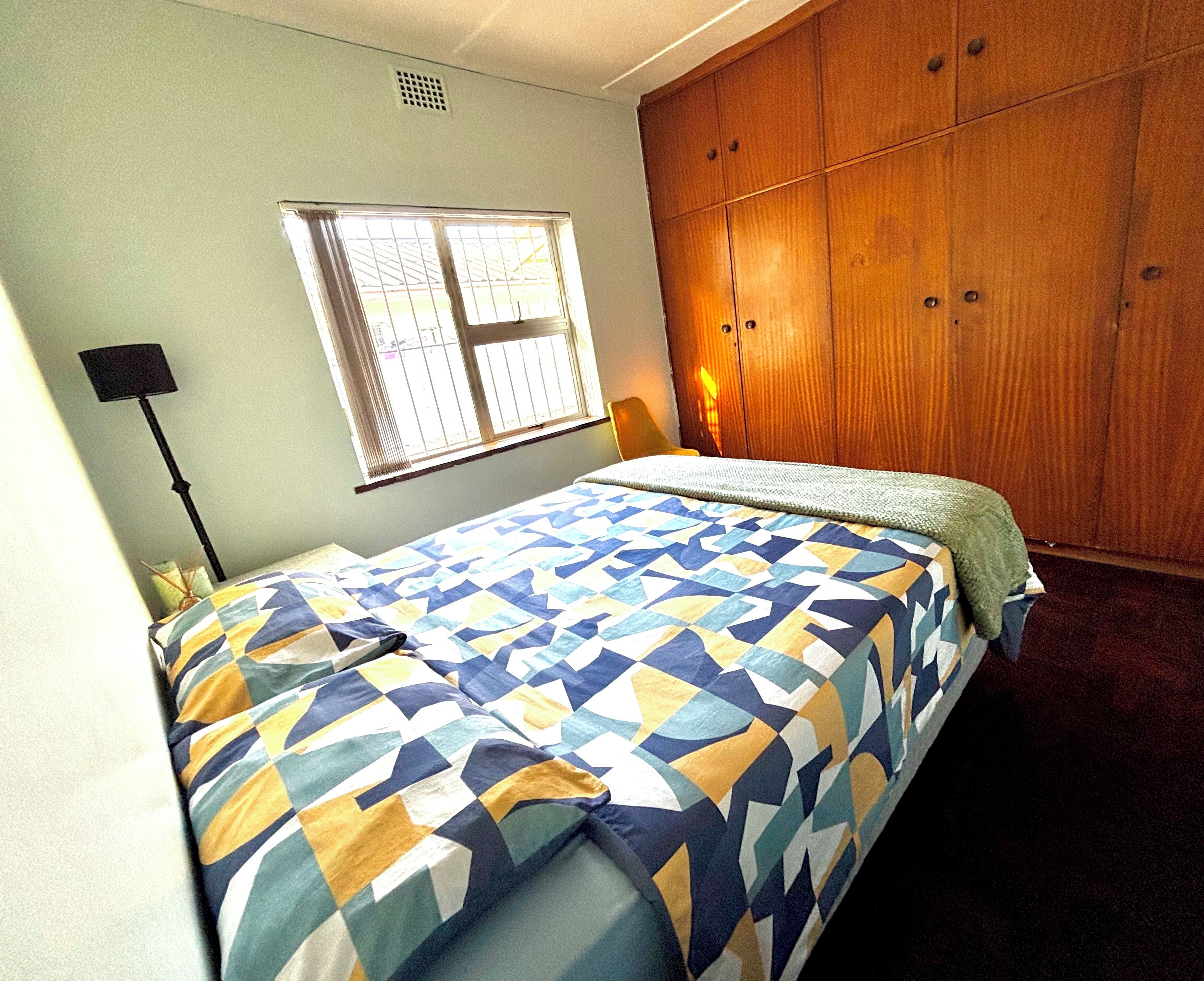 A bedroom with a bed, a window, a wardrobe, and a floor lamp.