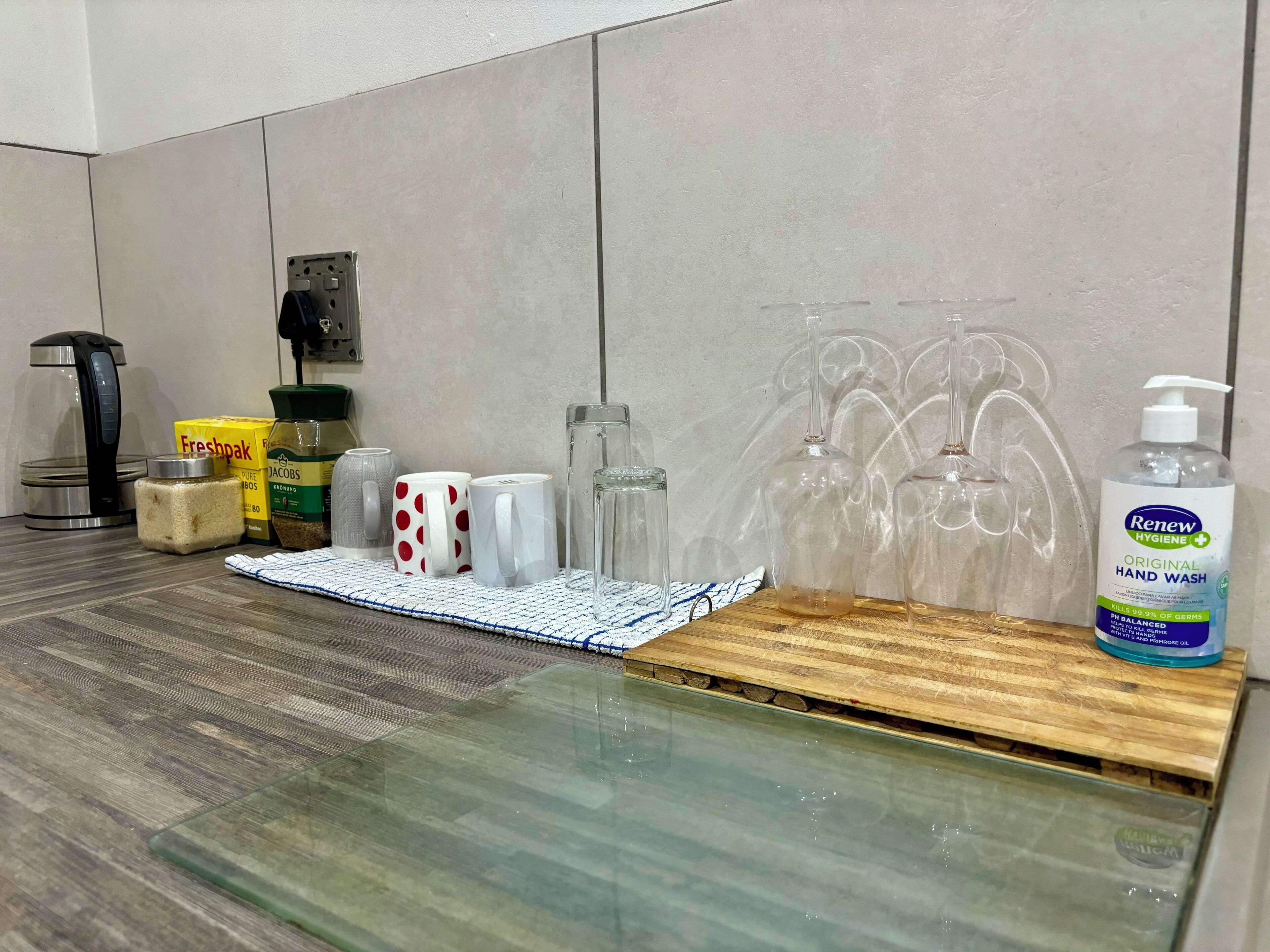 A kitchen counter with a coffee maker, a box of Freshpak, a jar of sugar, and a bottle of Renew Hygiene hand wash.