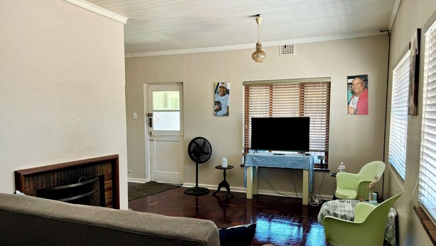 Una sala de estar con un sofá, una silla verde, un televisor sobre un mueble bajo y un ventilador.