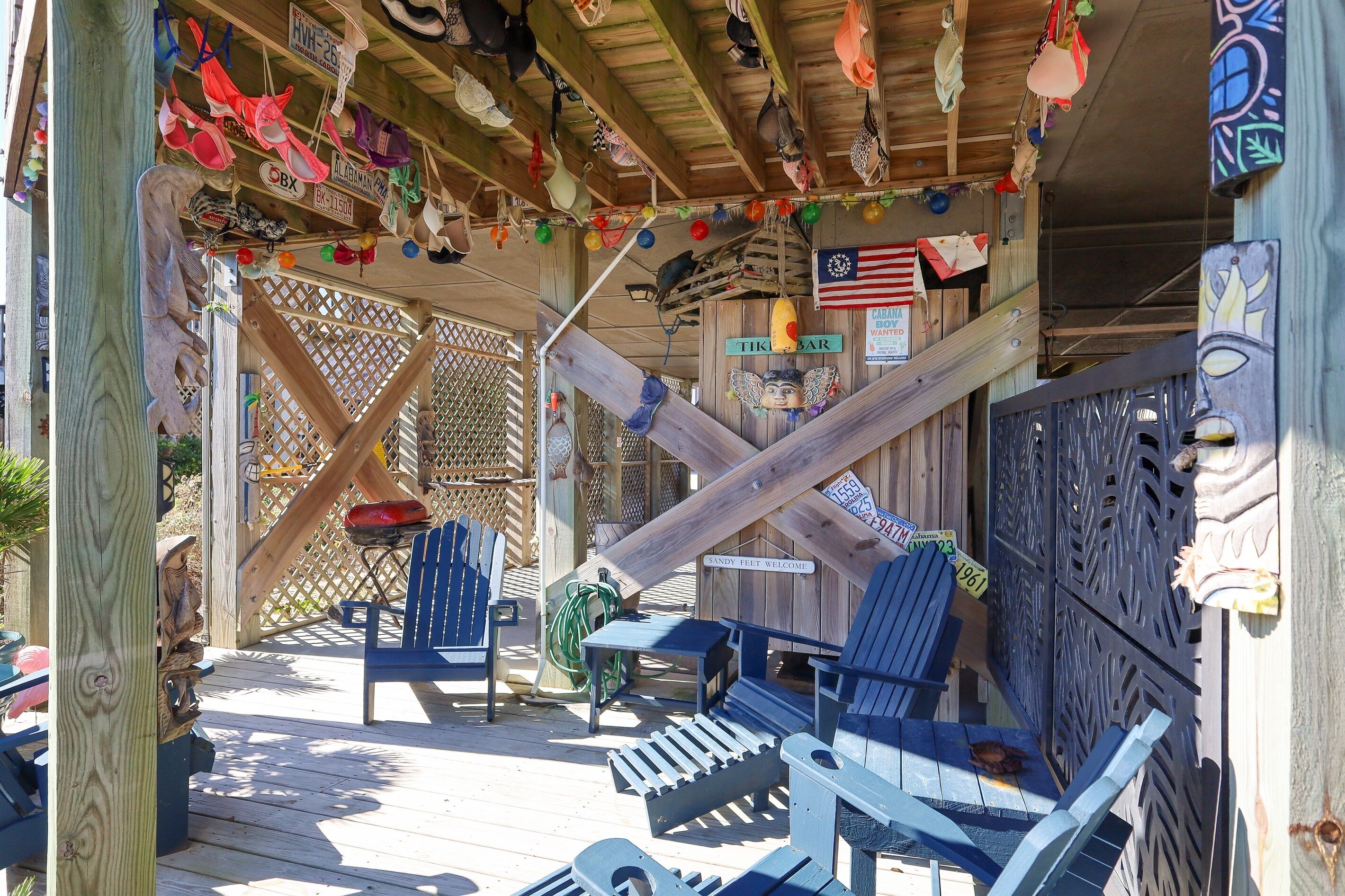 A wooden deck with Adirondack chairs, a small table, and a sign reading "Tiki Bar".