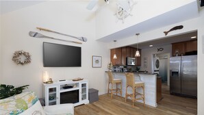A modern kitchen with wooden cabinets, a stainless steel refrigerator, and a bar area with wicker chairs. - Coastal Charm Awaits in Tiki Time on Topsail! (North Topsail Beach)