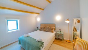 Ein Schlafzimmer mit Bett, Nachttisch, Lampe, Spiegel und Fenster.