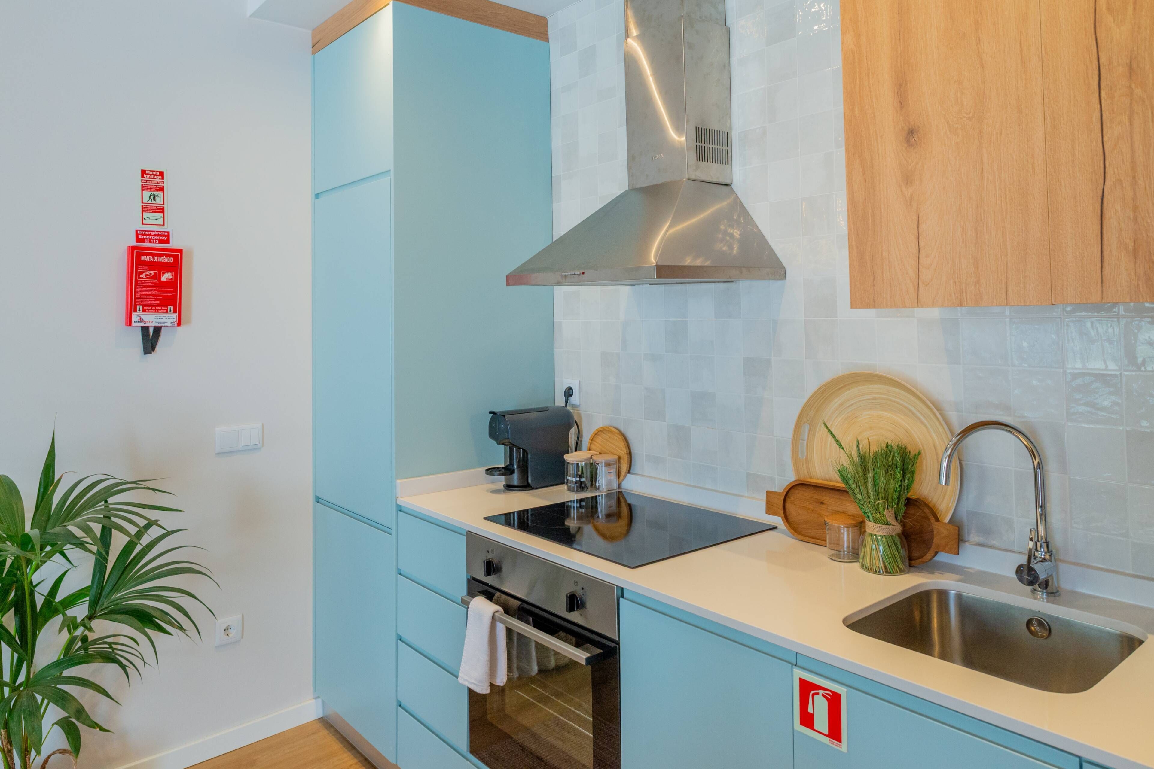 A modern kitchen with light blue cabinets, a stainless steel range hood, a built-in oven, a sink, and a coffee maker.