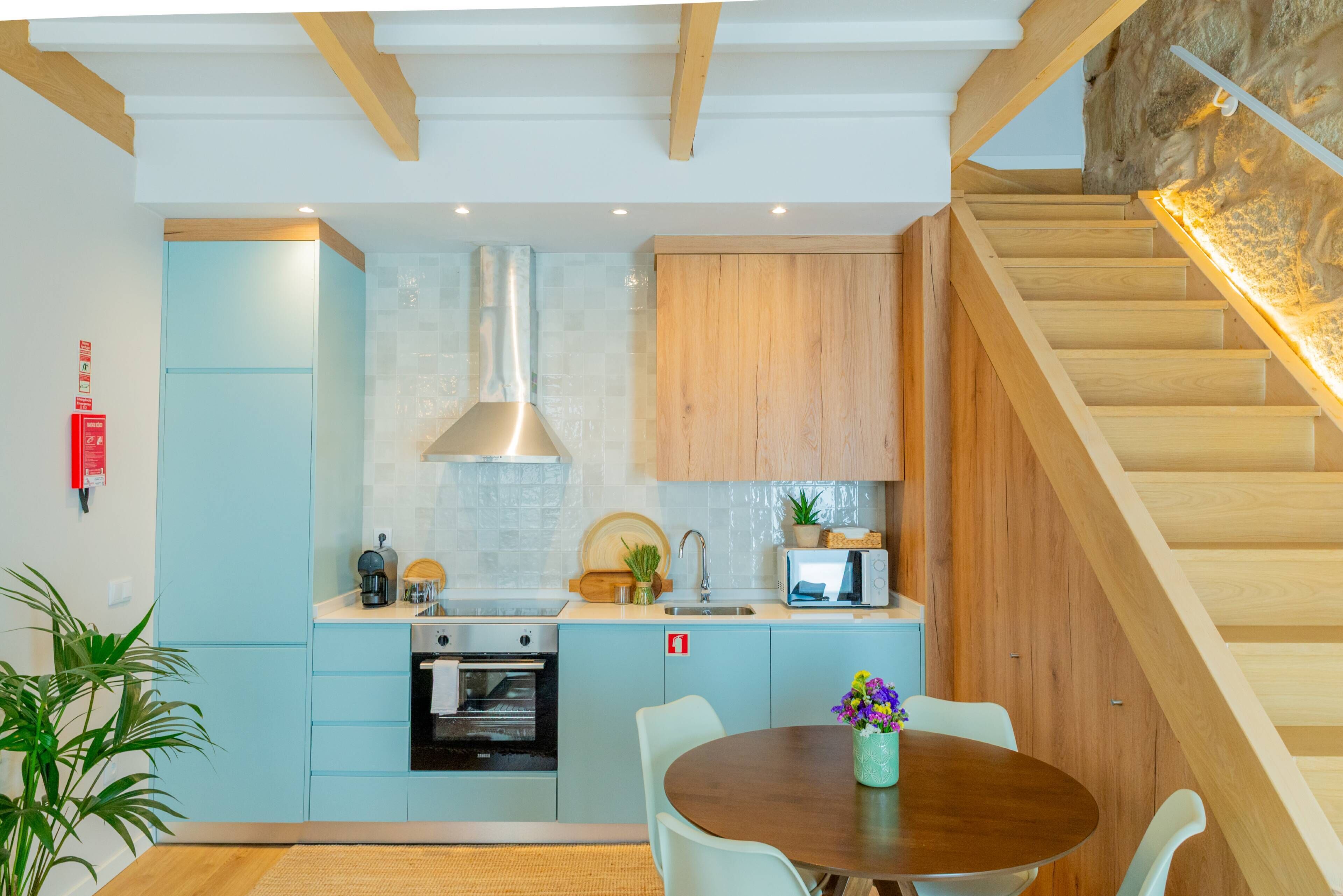 Een moderne keuken met lichtblauwe kastjes, een houten trap en een eethoek met een ronde tafel en stoelen.