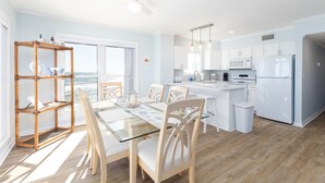 A modern kitchen with white cabinets, a central island, and a dining area with a glass table and chairs. - Coast is Clear– Oceanfront Escape at Topsail Dunes (North Topsail Beach)