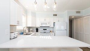 A modern kitchen with white cabinetry, a large island, and pendant lighting. - Coast is Clear– Oceanfront Escape at Topsail Dunes (North Topsail Beach)
