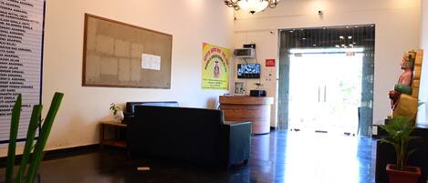 A reception area with a black sofa, a wooden reception desk, a chandelier, and a large poster on the wall.