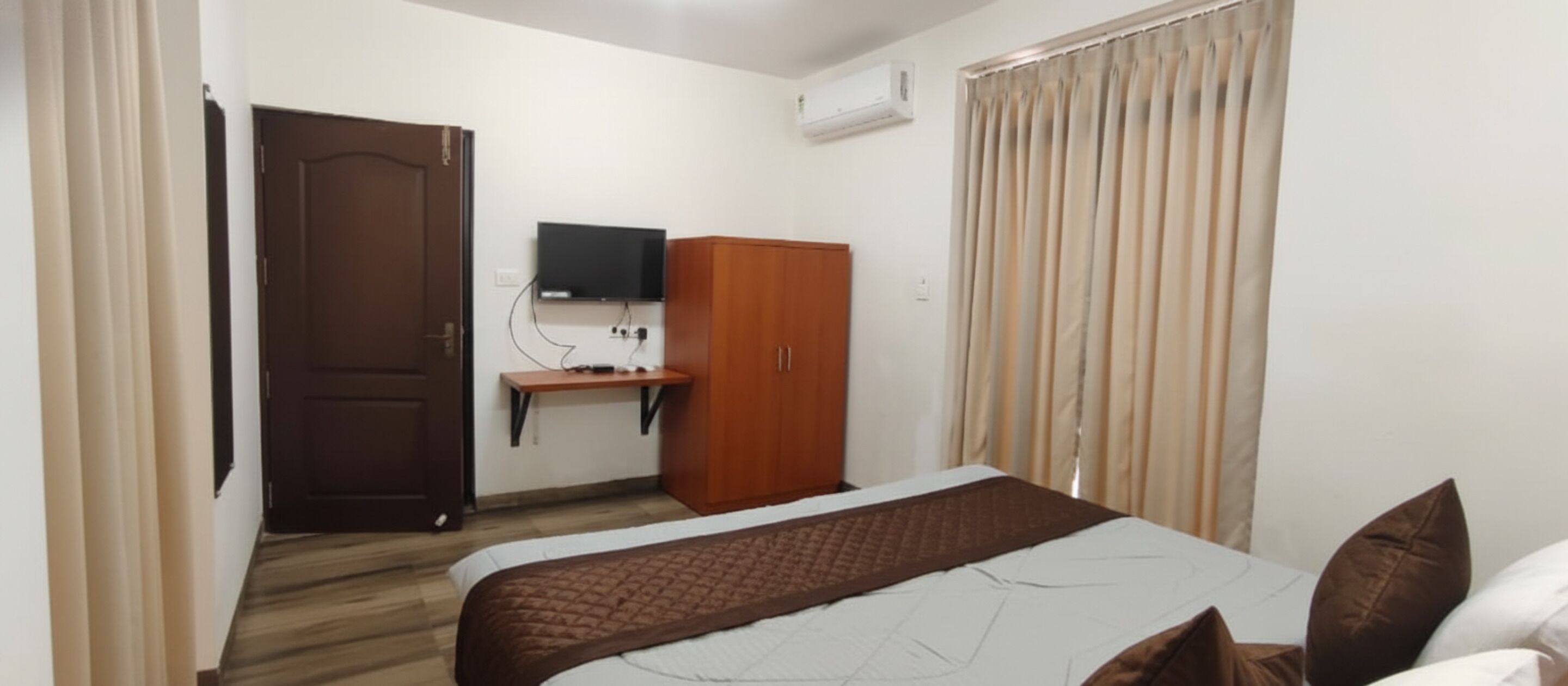Quarto de hotel com cama, guarda-roupa, secretária e televisão, e aparelho de ar condicionado.