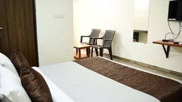 A hotel room with a bed, a desk, two chairs, a television, and a small table.