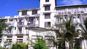 Un immeuble résidentiel à plusieurs étages, doté de balcons et de climatiseurs, avec un ciel bleu dégagé.