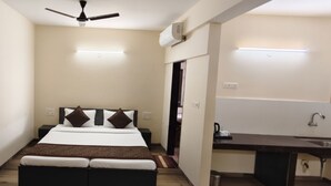 Une chambre comprenant un lit, des tables de chevet, un ventilateur de plafond, un appareil de climatisation et une kitchenette équipée d’un évier et d’un plan de travail.