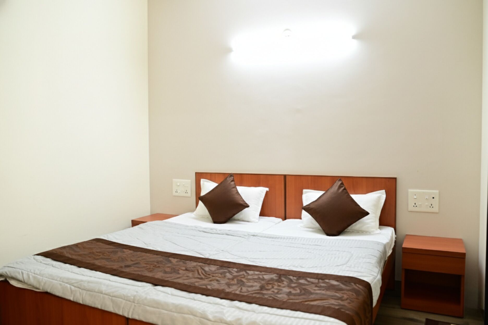 A neatly made bed with a patterned bedspread, two pillows, and a bedside table with a lamp.