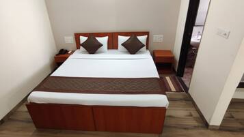 A neatly made bed with a wooden headboard, a bedside table with a phone, and a nightstand with a lamp.