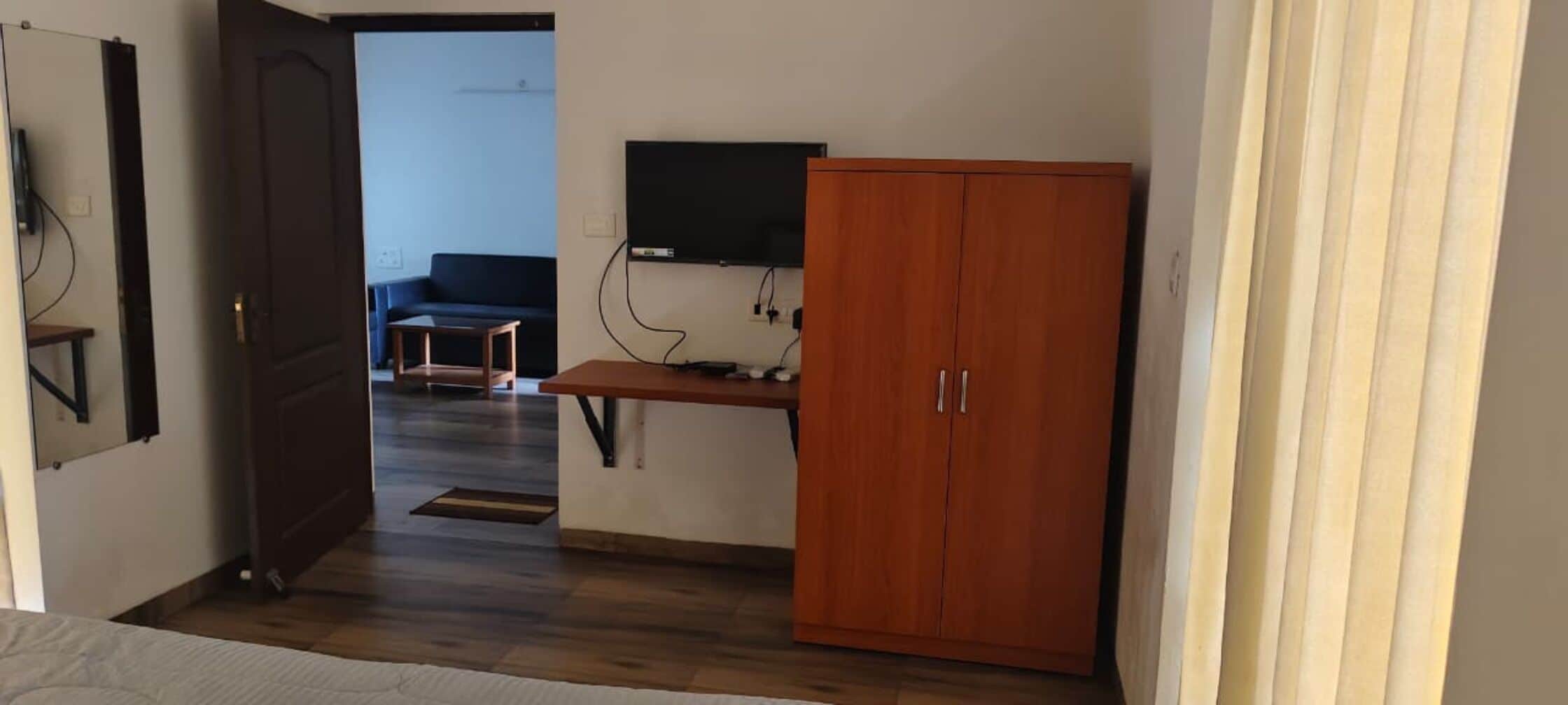 Una habitación con un armario de madera, un escritorio con ordenador y una televisión en la pared.